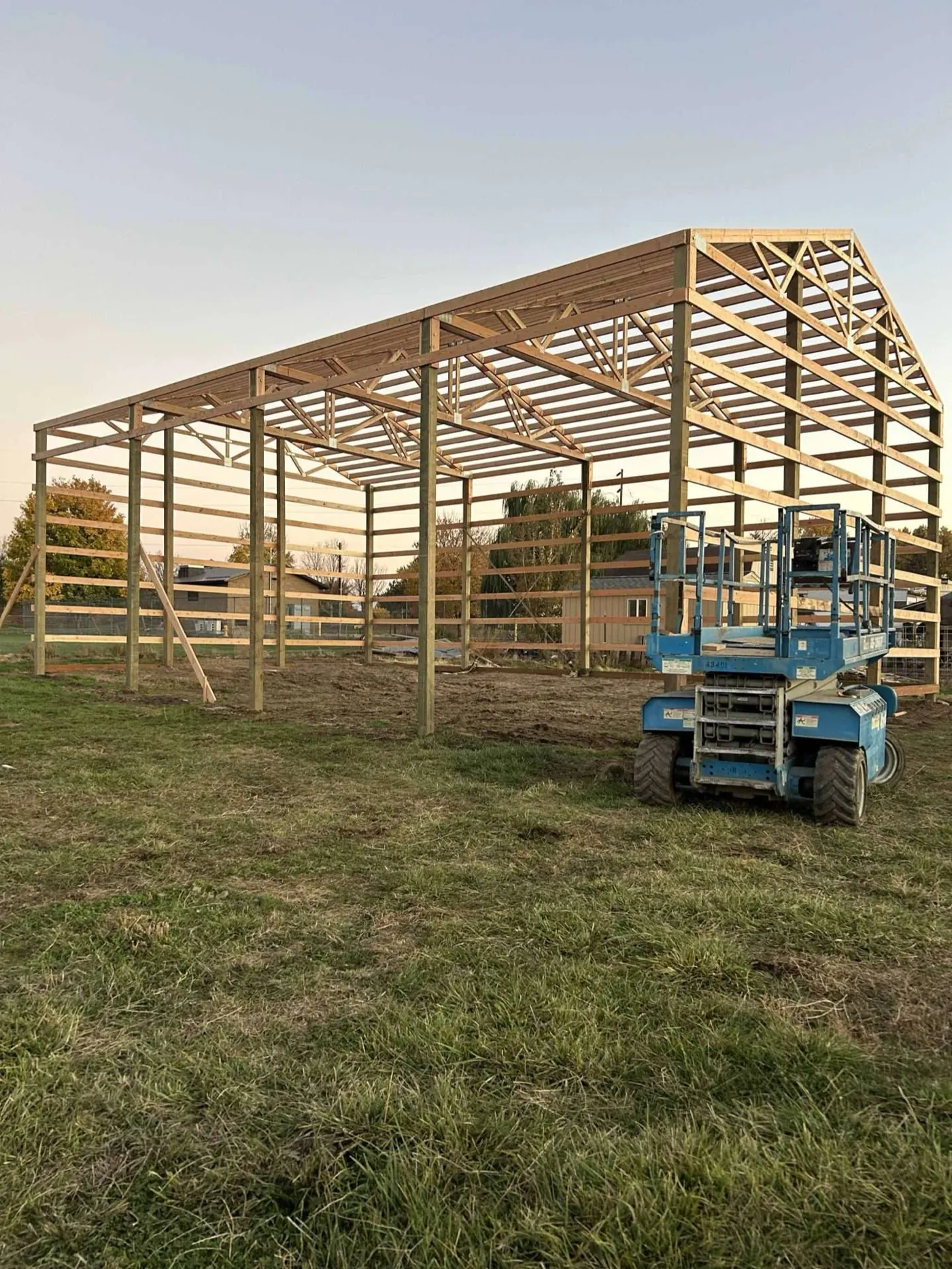 Pole building frame fully raised, viewed at dusk with a scissor lift on site