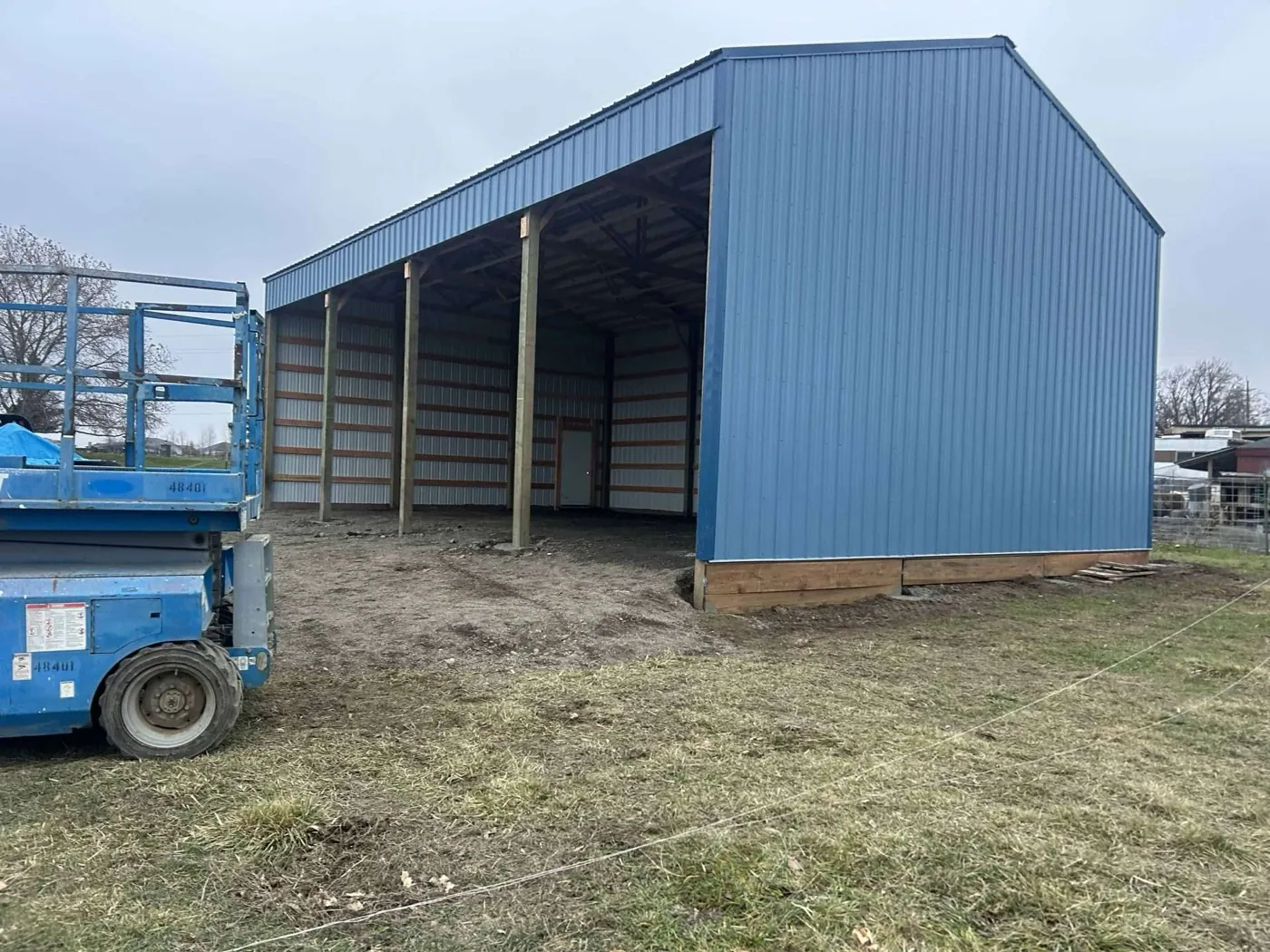Finished pole building with blue metal roofing and panel siding, open bay on one end