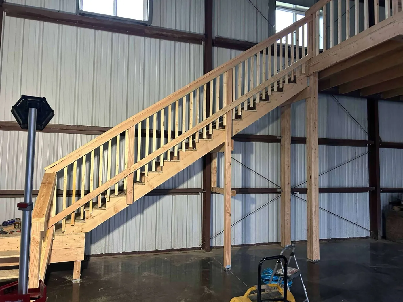 Framed interior staircase built inside a steel building, with two installed windows visible above