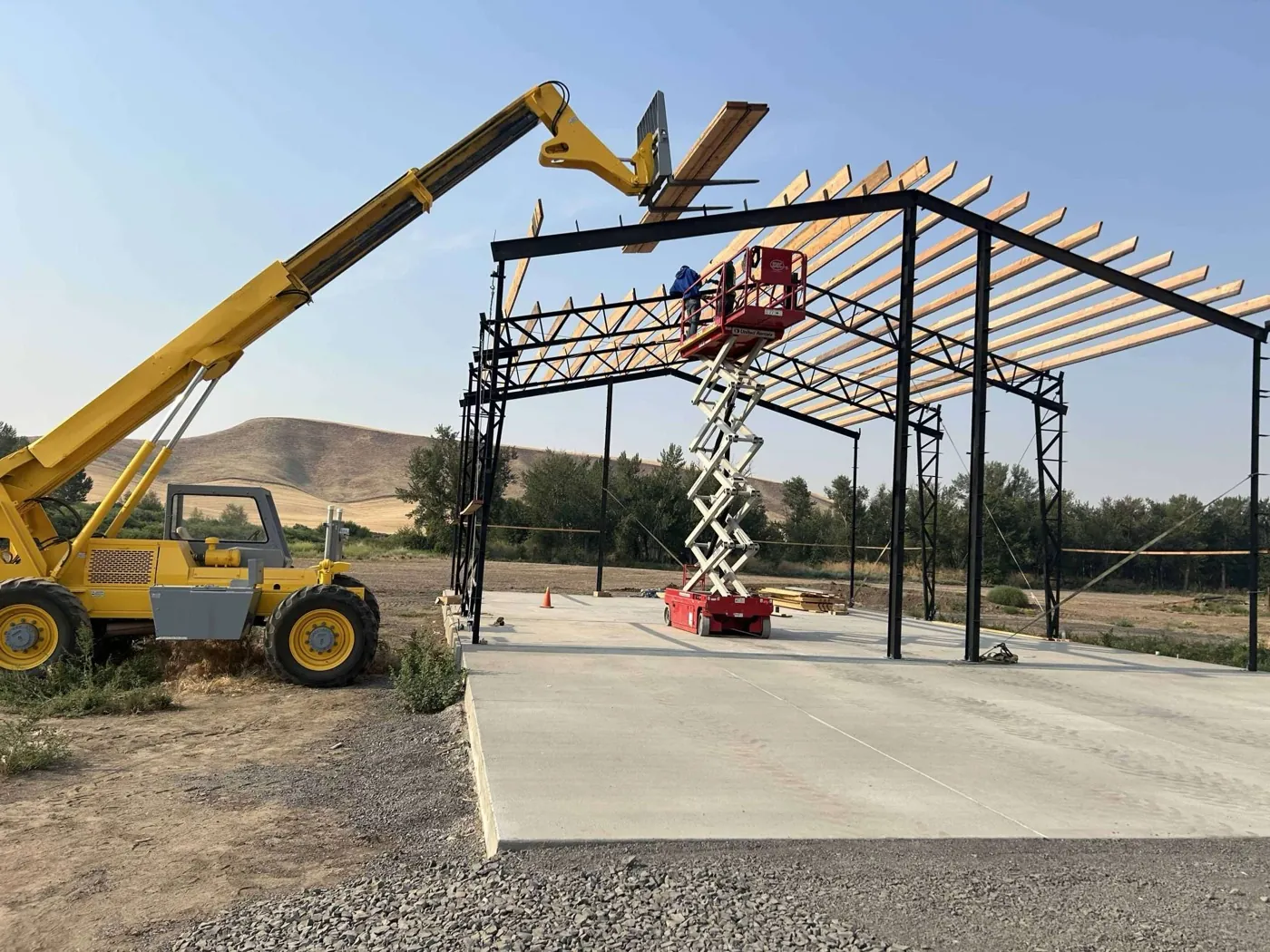 Crew erecting a steel-frame structure on a wheat-country lot